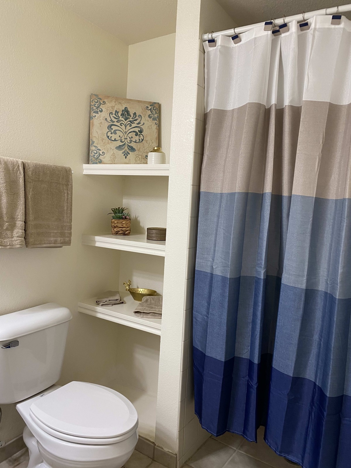 A neatly organized bathroom with a blue gradient shower curtain and decorative shelves.