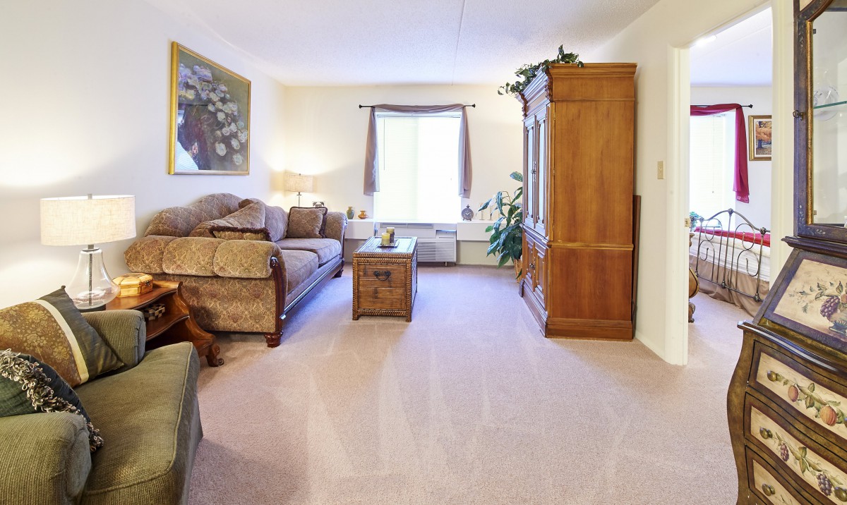 A cozy living room with a sofa, coffee table, and cabinet, featuring a large window and artwork on the wall.