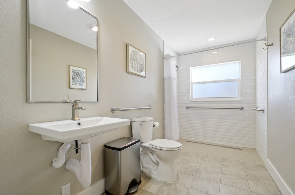 A modern bathroom with a sink, toilet, and large mirror, featuring minimalist decor.