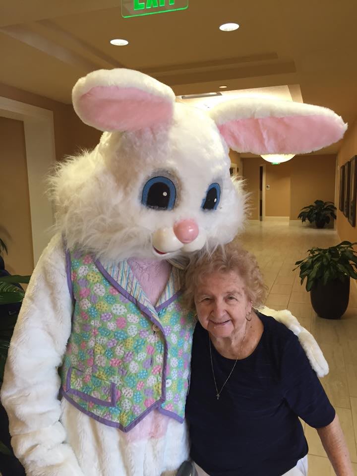 An elderly woman posing with the Easter Bunny indoors.