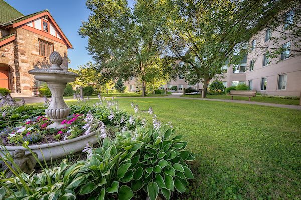 A picturesque garden with a fountain surrounded by flowers and lush greenery in a residential area.