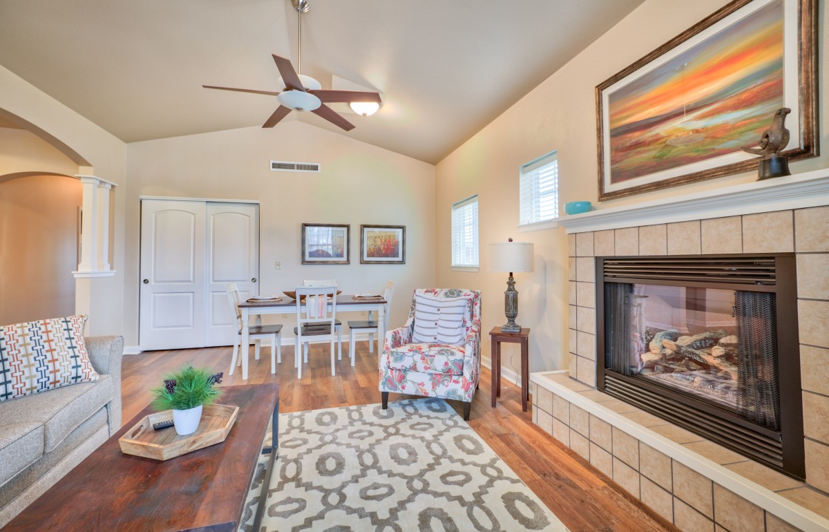 A cozy living room featuring a fireplace, ceiling fan, and stylish decor with a view into the dining area.