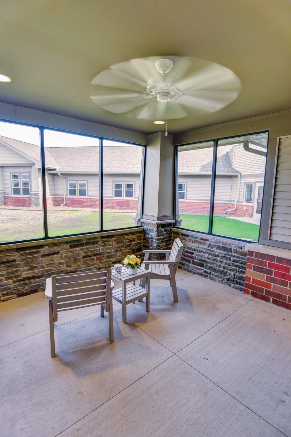 A cozy screened porch with a ceiling fan, featuring two chairs and a small table.