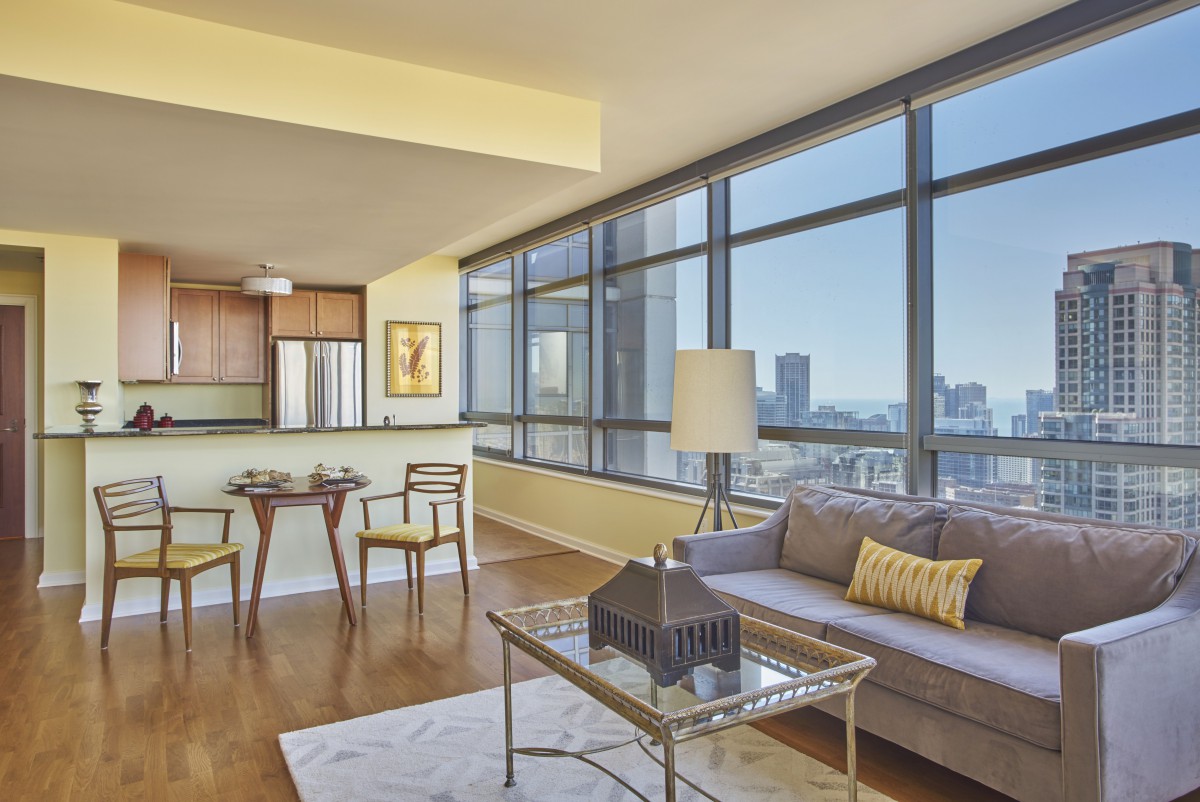 A modern living room with large windows offering a city view, featuring contemporary furniture and decor.