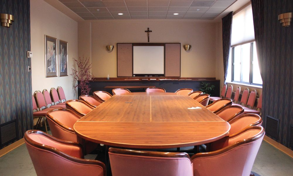 A conference room with a large meeting table, surrounded by chairs and featuring a projector screen and decorative elements.