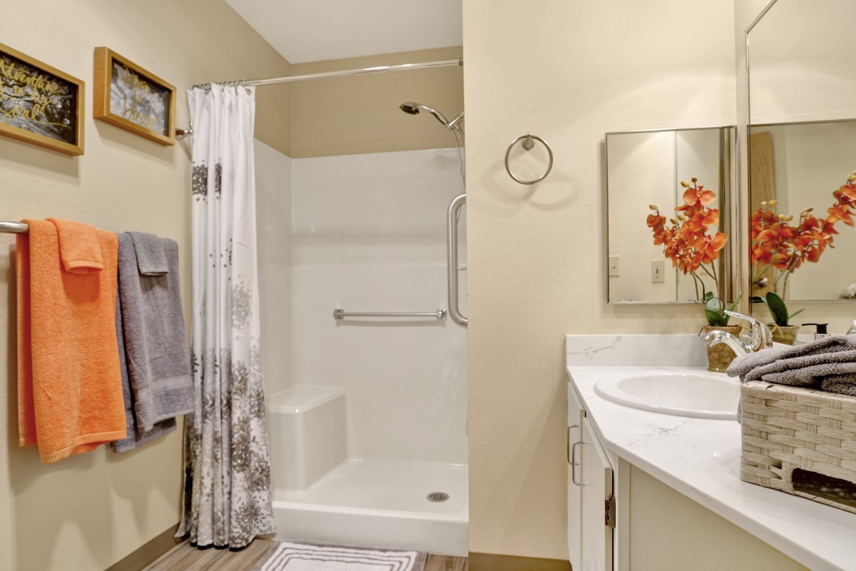 A clean and modern bathroom featuring a shower with a curtain, towels, a sink with a mirror, and decorative flowers.