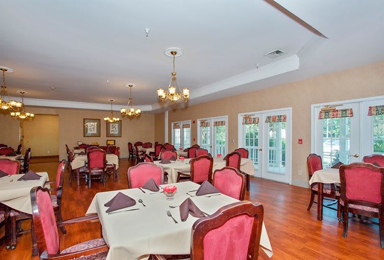 An elegantly set dining room with neatly arranged tables and chairs, adorned with chandeliers.
