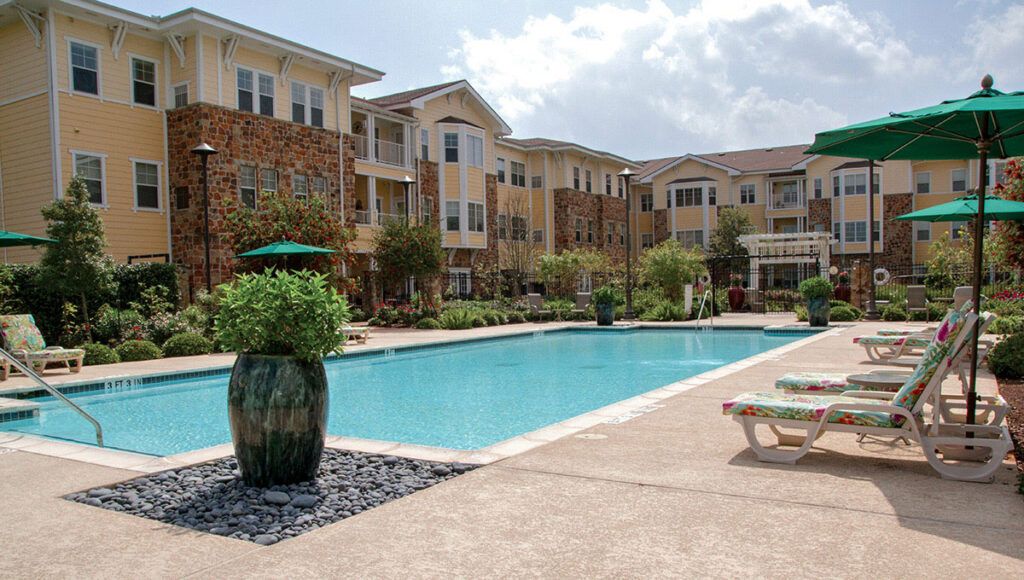A modern apartment complex with an inviting outdoor swimming pool surrounded by lush landscaping.