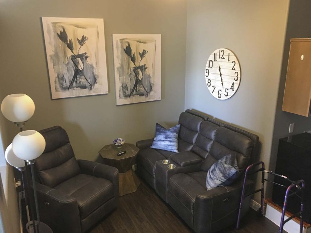 A cozy living room with a comfortable sofa, armchair, wall clock, and abstract artwork.