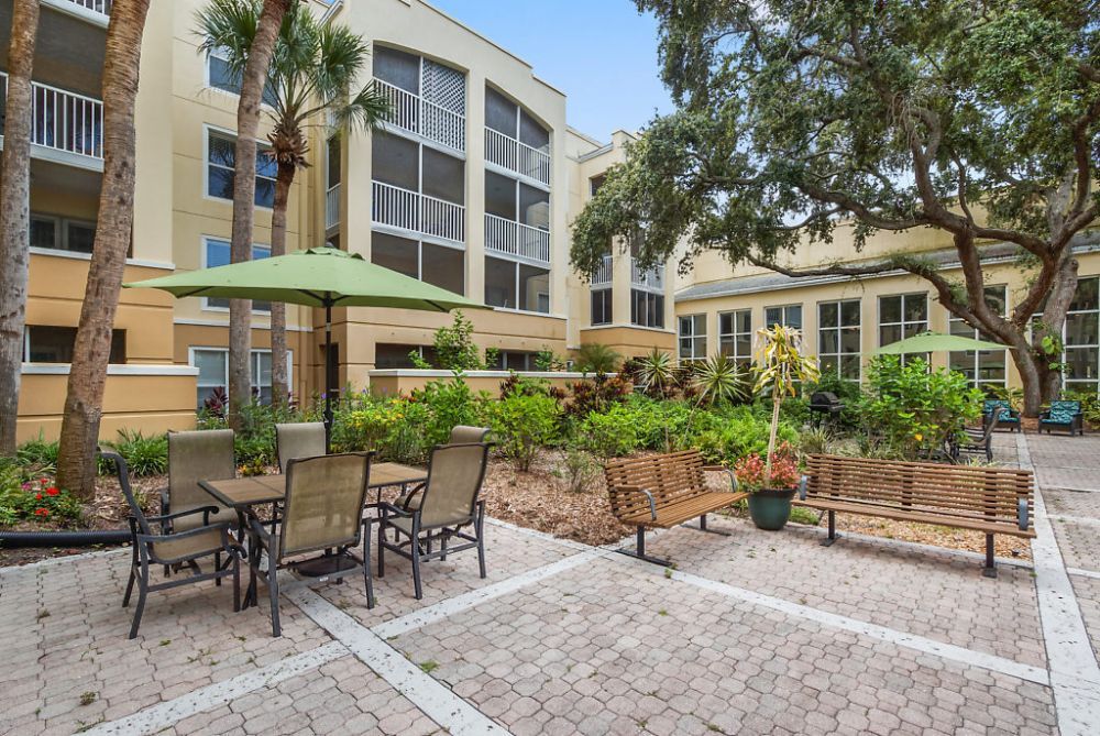A well-maintained outdoor patio with tables, chairs, and garden beds, adjacent to a residential building.