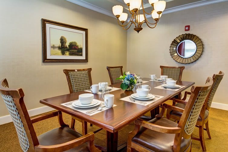 A beautifully set dining room table with a chandelier overhead, featuring elegant place settings and a centerpiece of flowers.