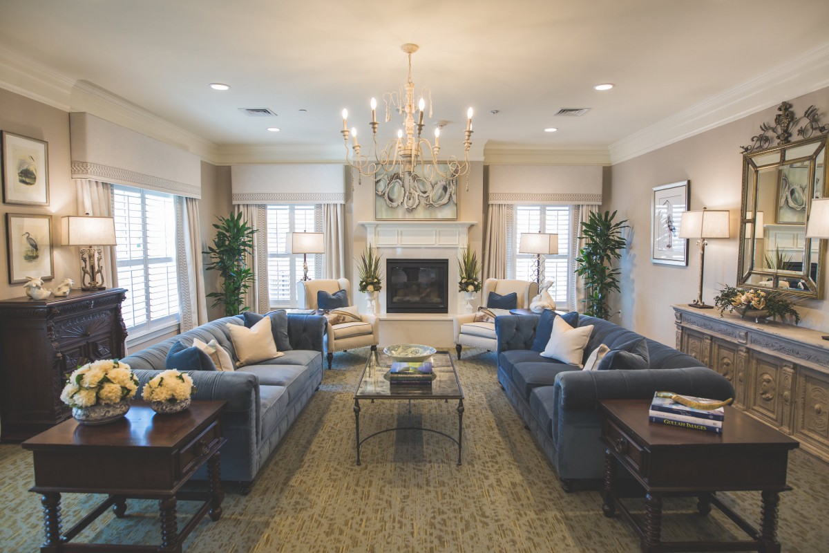 A spacious and elegantly designed living room featuring plush sofas, a central chandelier, and a cozy fireplace.