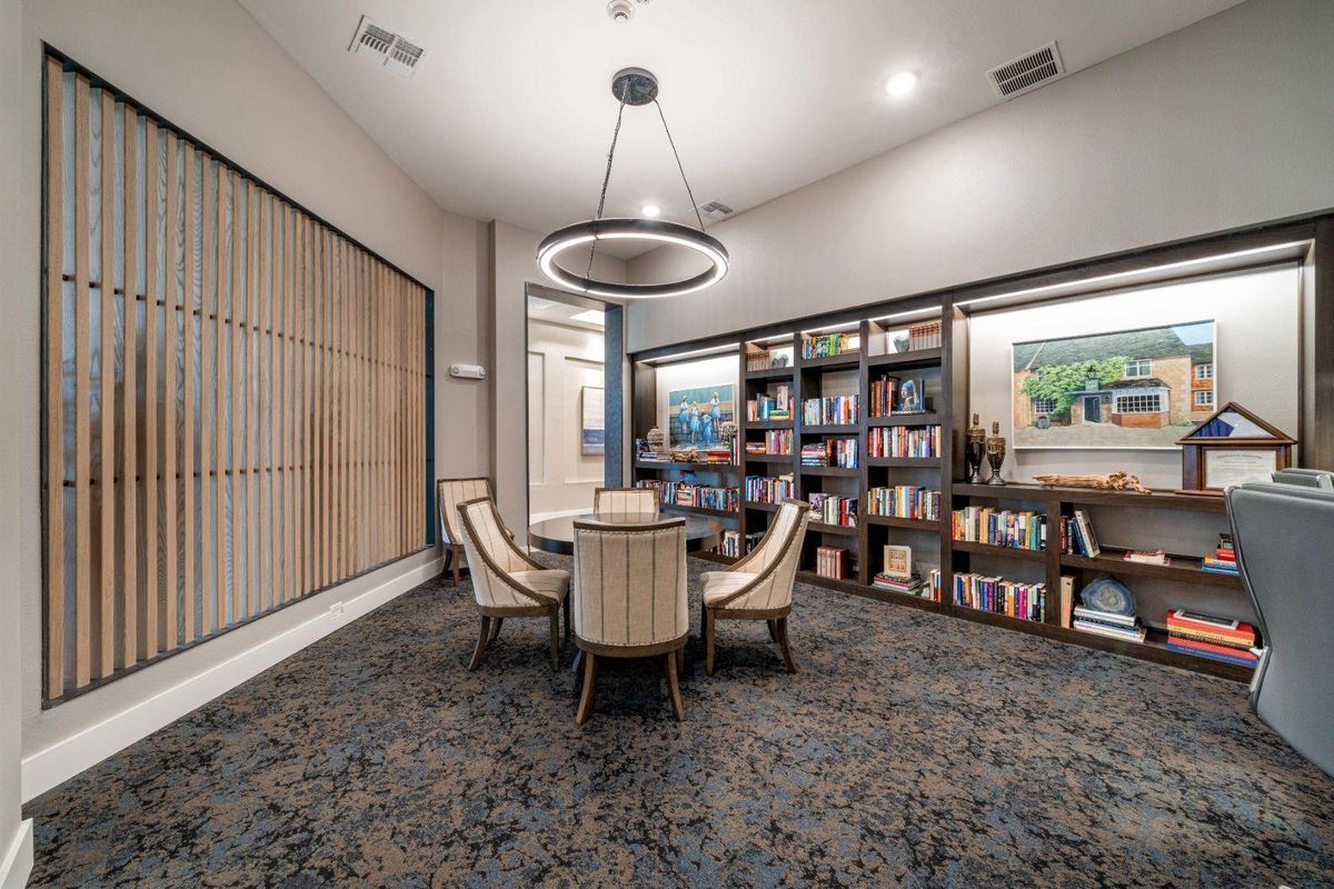 A modern library room with a round table and chairs, surrounded by bookshelves and illuminated by a stylish chandelier.