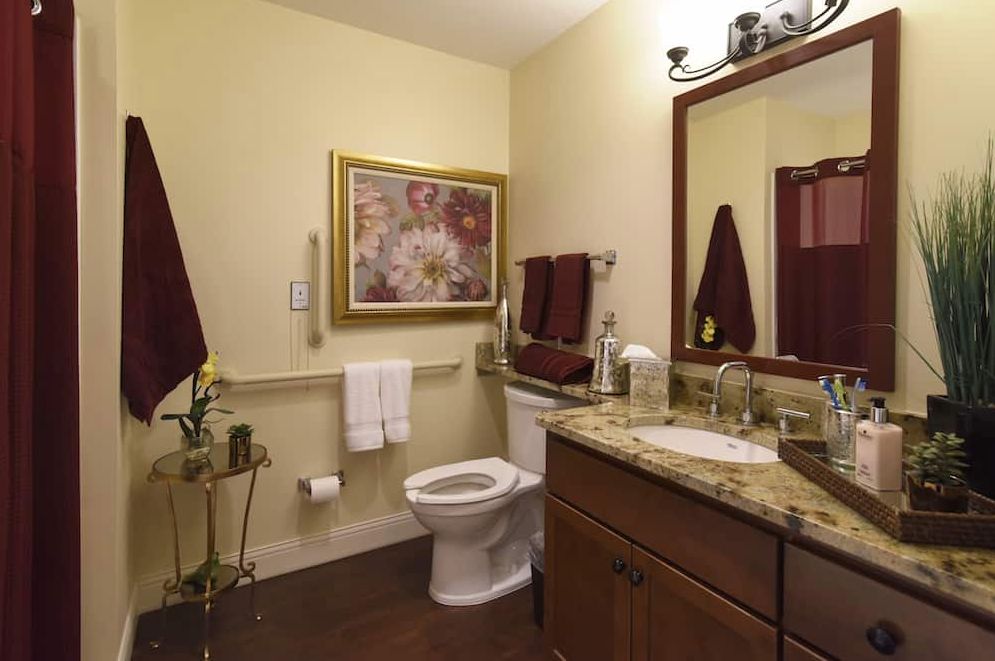 A cozy bathroom with a granite countertop, wall art, and red towel accents.