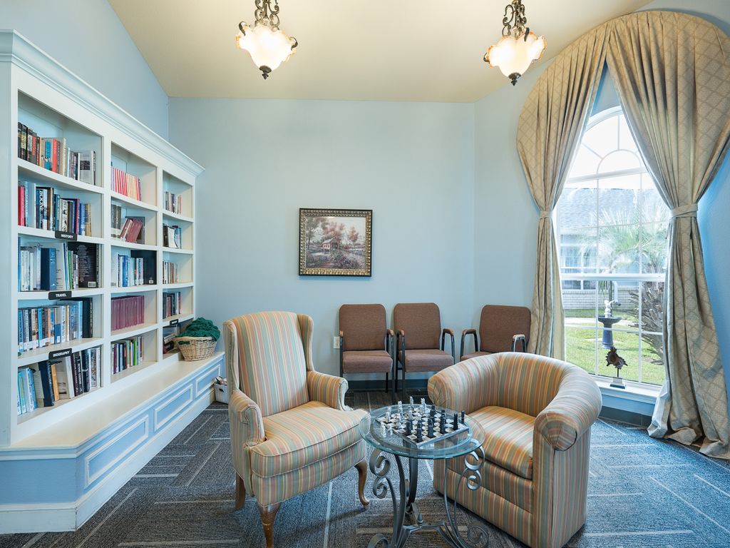 A cozy library room with armchairs, a chess table, and a large window.