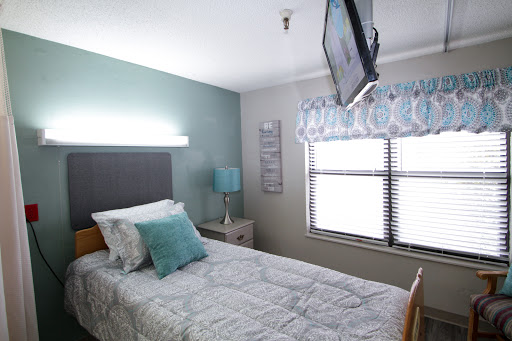 A cozy and modern bedroom featuring a single bed, television, and natural light from the window.