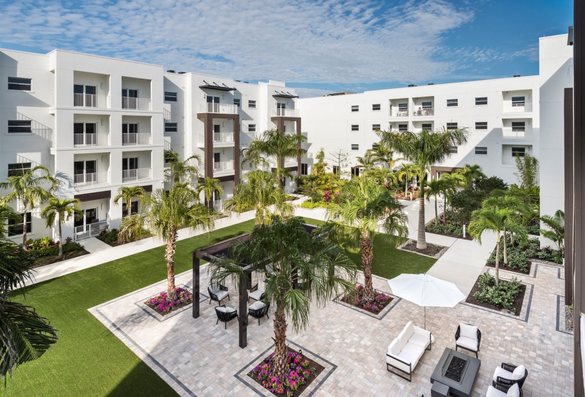 A modern apartment complex featuring a beautifully landscaped courtyard with outdoor seating and palm trees.