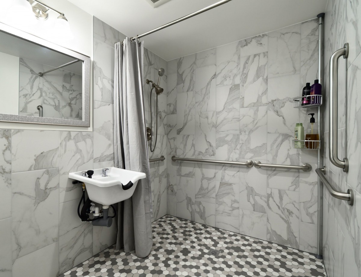 An accessible bathroom with marble tiles, featuring a shower area with a curtain and grab bars for support.