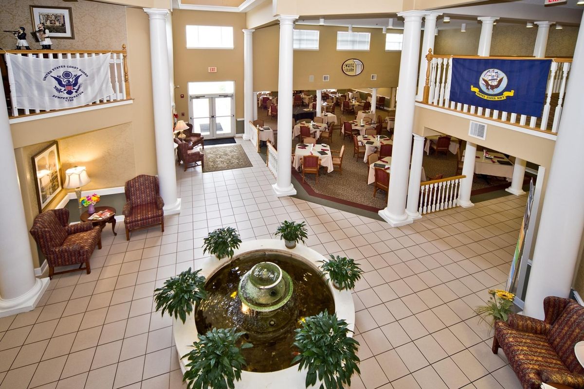 A spacious lobby featuring a central fountain, surrounded by plants and seating, with an open atrium design and visible dining area.
