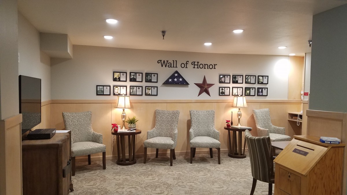 A 'Wall of Honor' displays framed photographs and patriotic decorations, accompanied by a row of chairs and lamps in a warmly lit room.