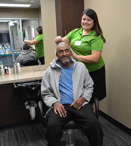 A cheerful hairstylist provides a haircut to an elderly man in a salon setting.