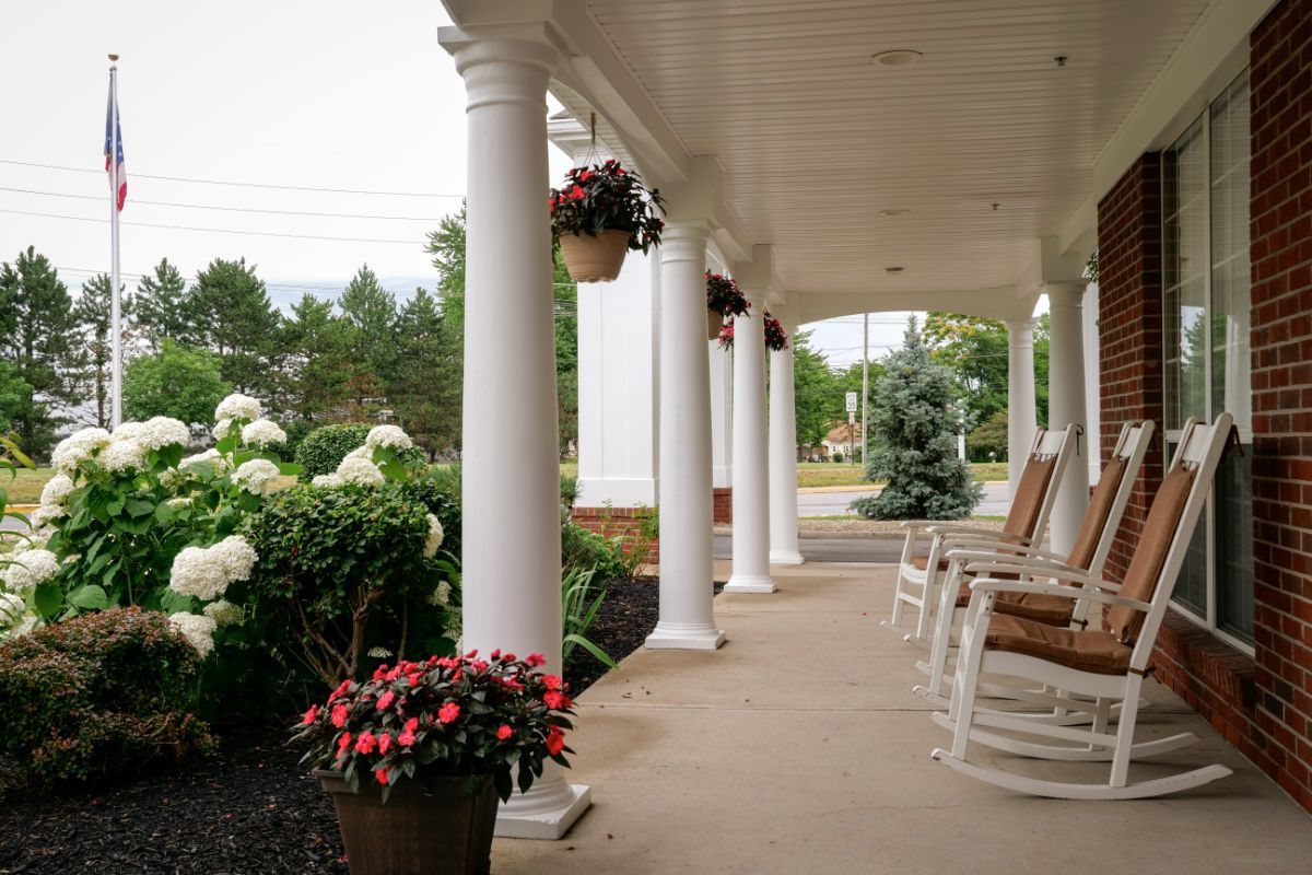 A serene porch with white columns, rocking chairs, and vibrant flower arrangements.