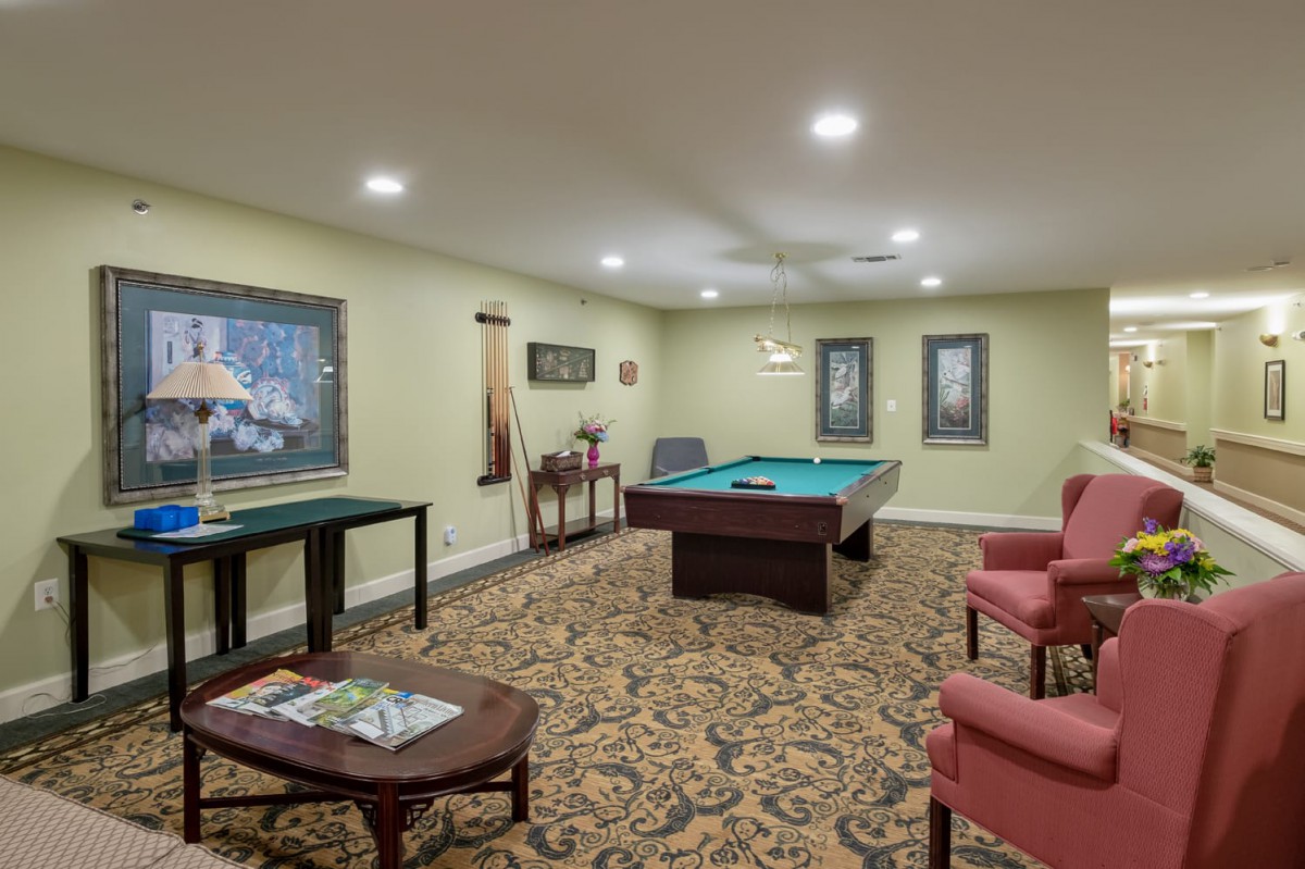 A cozy game room featuring a pool table and comfortable seating, adorned with artwork and a patterned carpet.