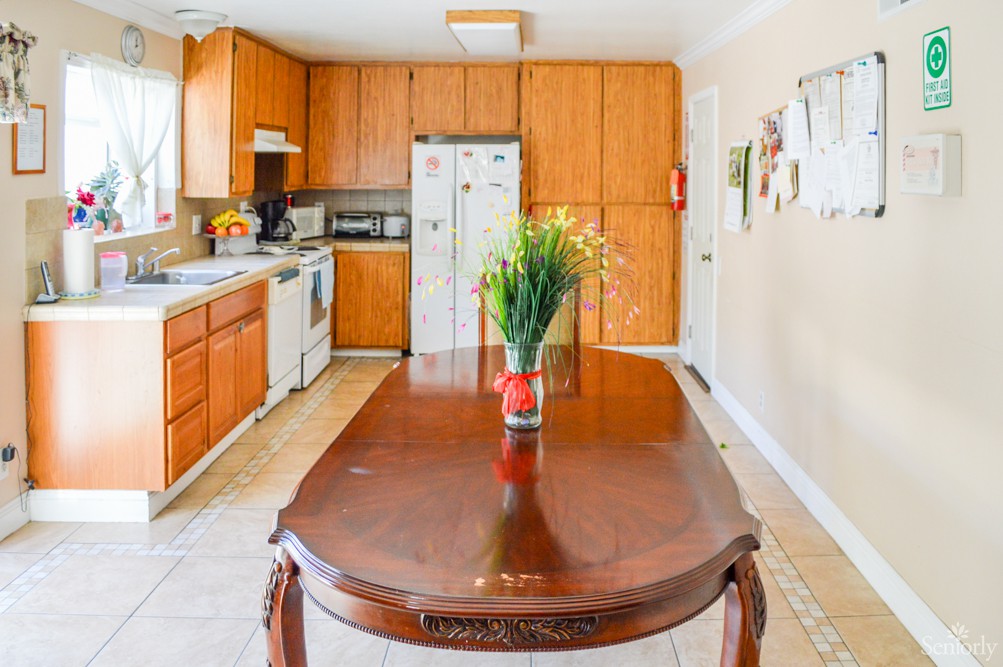 A bright kitchen with wooden cabinets and a dining table featuring a flower vase centerpiece.