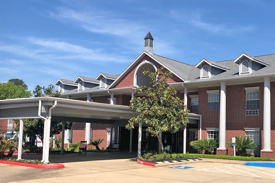 A brick building with white columns and a covered entrance on a sunny day.