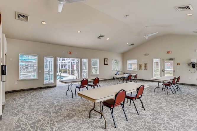 A spacious community room with tables and chairs, well-lit by natural light through large windows.