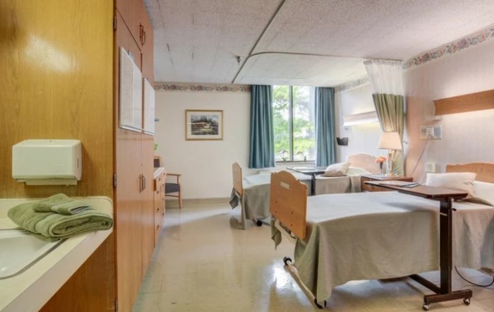 A shared hospital room with two beds, equipped with essential furniture and a window providing natural light.