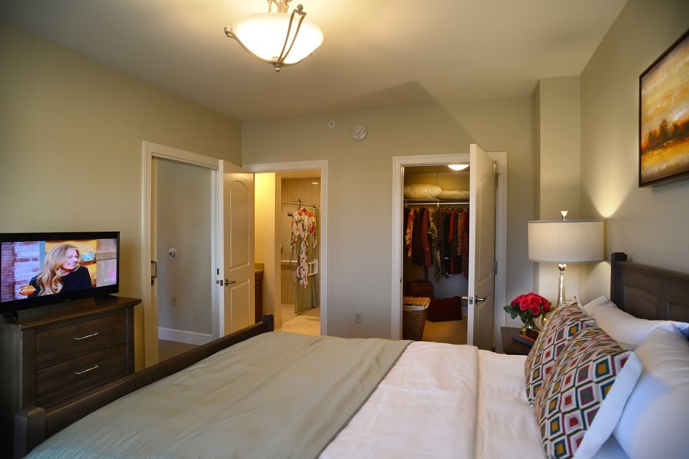 A cozy bedroom with a neatly made bed, television, and an open closet.