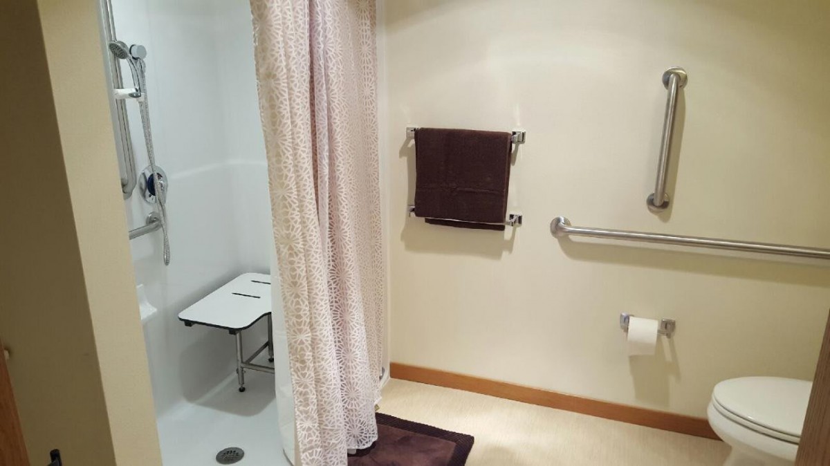 An accessible bathroom with a shower seat, handrails, and a towel rack.