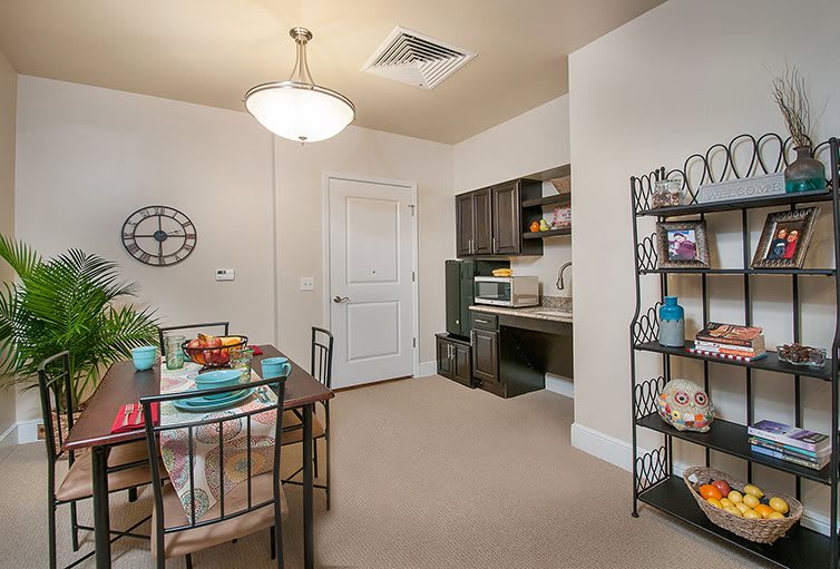 A small dining area with a table set for a meal, adjacent to a kitchen space featuring shelves and a microwave.