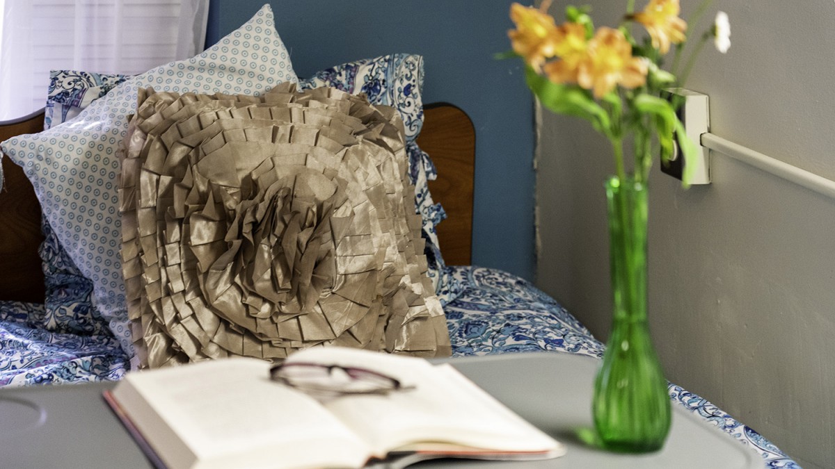 A cozy bedroom scene with an open book and glasses on the table, alongside a vase of flowers.