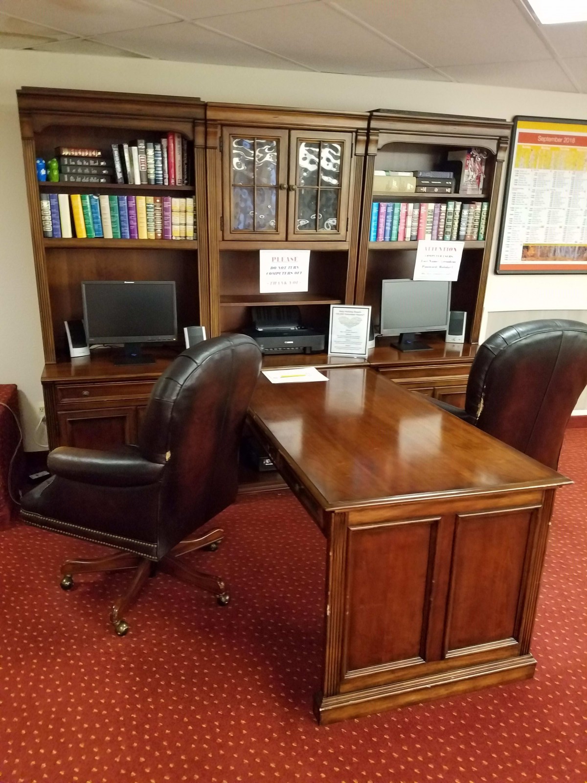 A well-organized office space featuring a wooden desk, leather chairs, bookshelves, and computers.