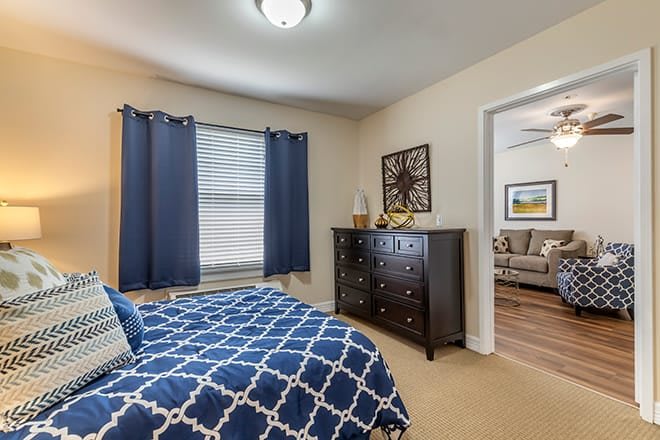 A cozy bedroom with blue curtains and a patterned bedspread, featuring a dark wood chest of drawers.