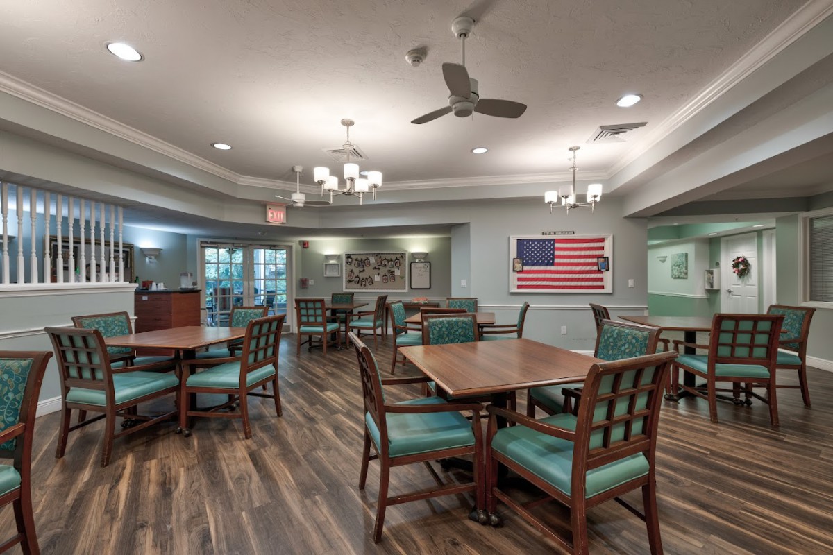 An inviting dining room with wooden floors, set with tables and chairs, featuring a prominent American flag on the wall.