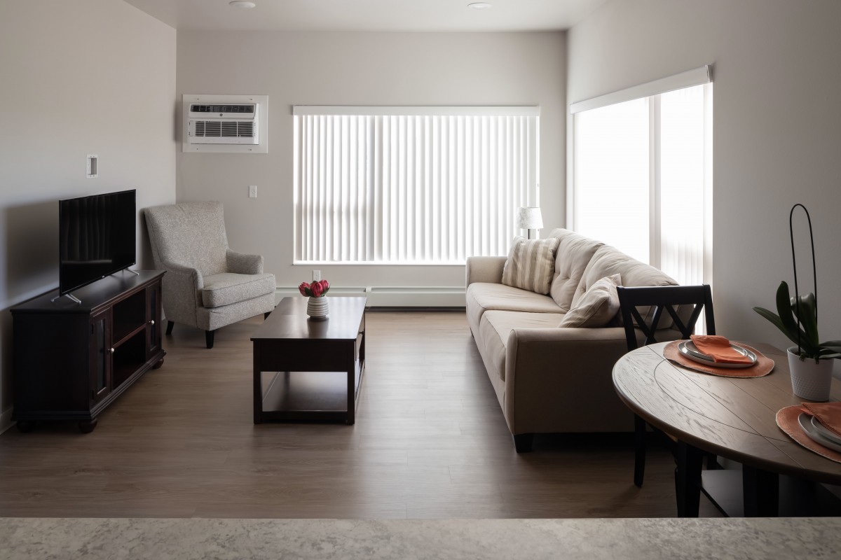 A minimalist living room featuring a sofa, armchair, and coffee table with large windows and vertical blinds.