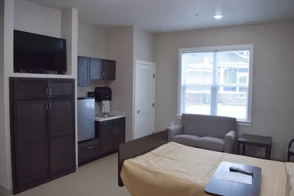 A cozy studio apartment with a bed, sofa, kitchenette, and TV.