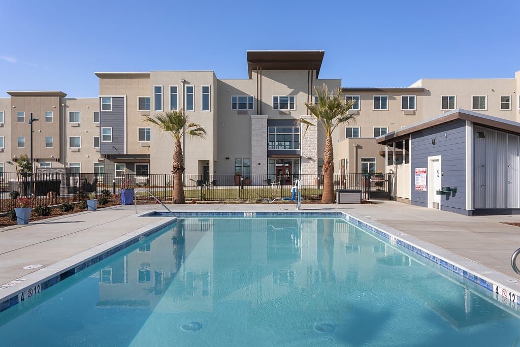 A modern apartment complex with a clear blue swimming pool and palm trees.