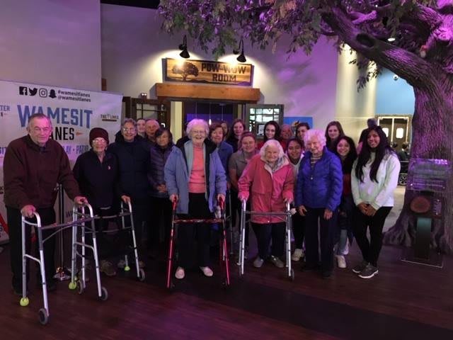 A group of seniors gathered indoors, some using walkers.