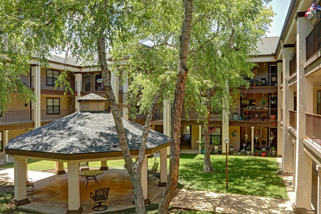 A peaceful courtyard featuring a gazebo surrounded by lush trees and a multi-story building.