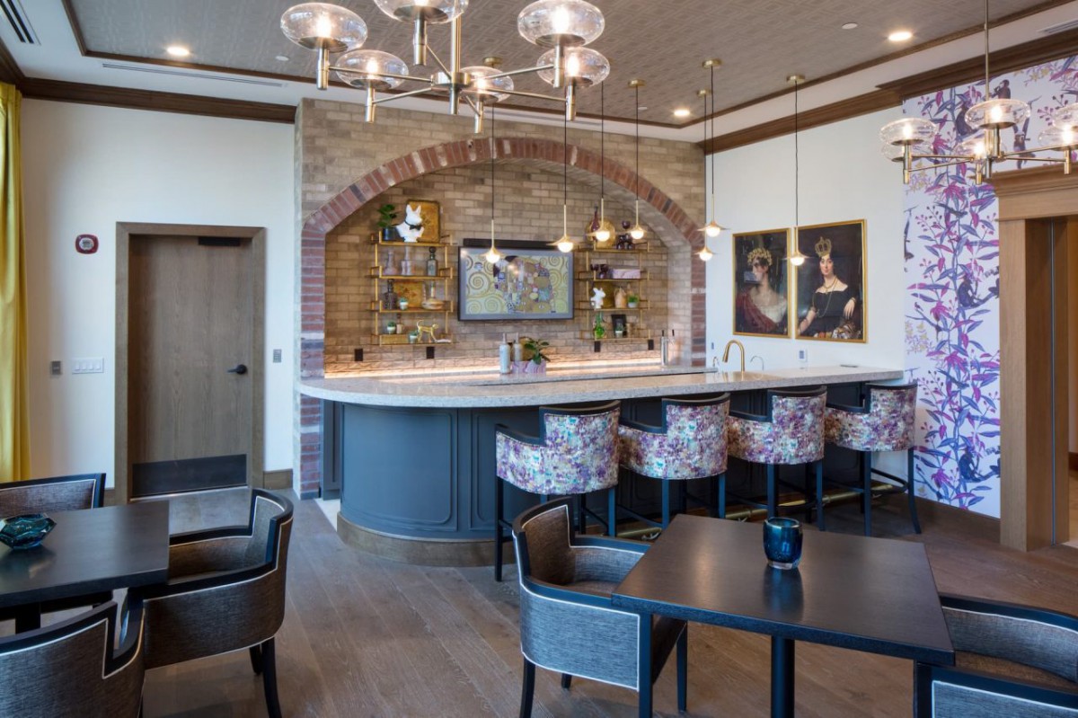 A modern bar area featuring a curved counter with stylish seating, chic chandeliers, and artwork on the walls.