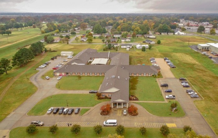 An aerial view of a large building complex with surrounding parking areas and green spaces in a suburban setting.