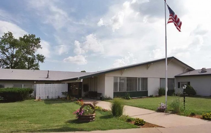 A single-story building with a flagpole and neatly landscaped grounds under a cloudy sky.