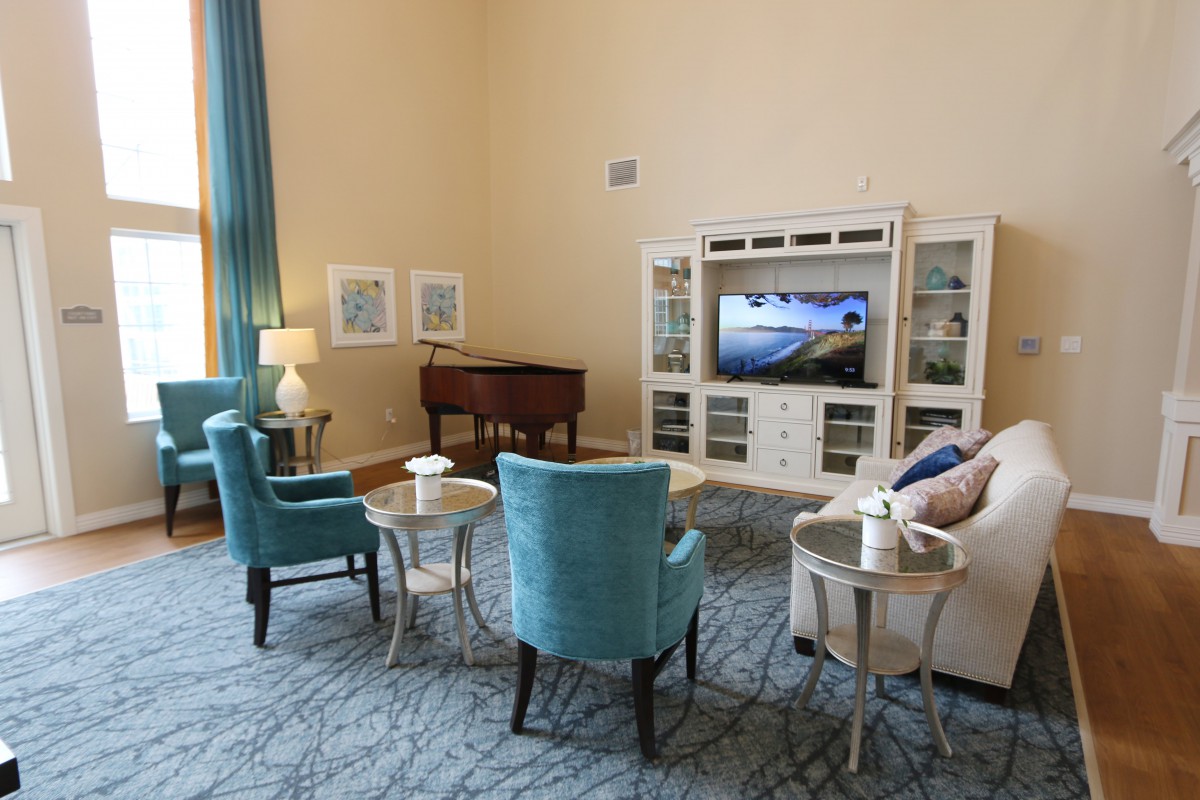 A cozy living room with elegant furniture, featuring a television, blue chairs, a couch, and a piano.