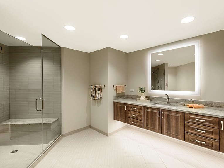 A modern bathroom featuring a glass shower, wooden vanity, and illuminated mirror.