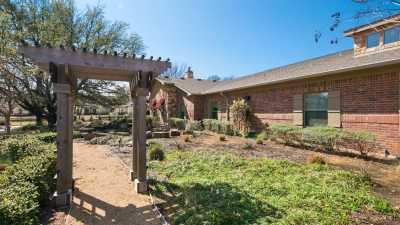 A beautiful garden with a pergola in front of a brick house on a sunny day.