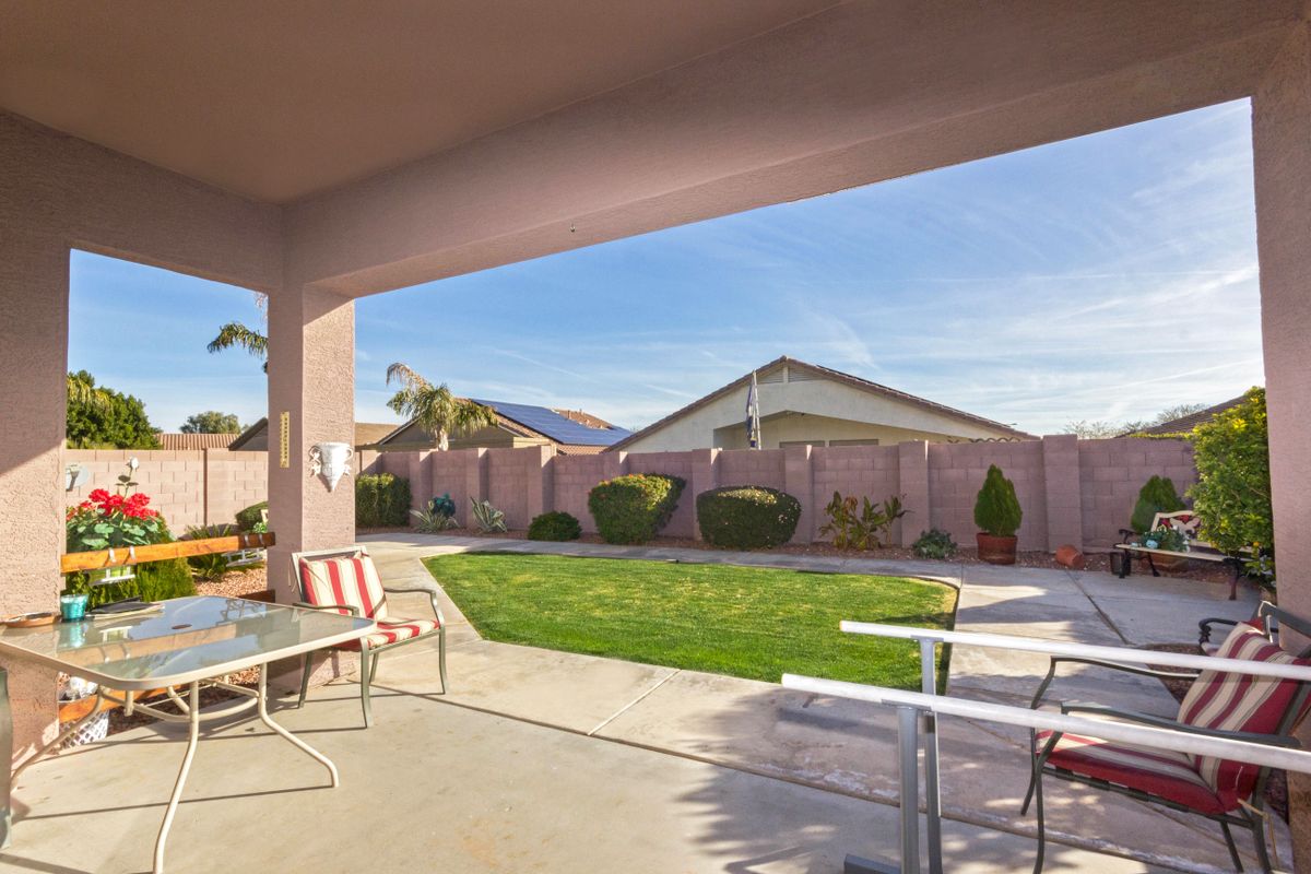 A sunny backyard featuring a patio with outdoor furniture and a well-maintained lawn.